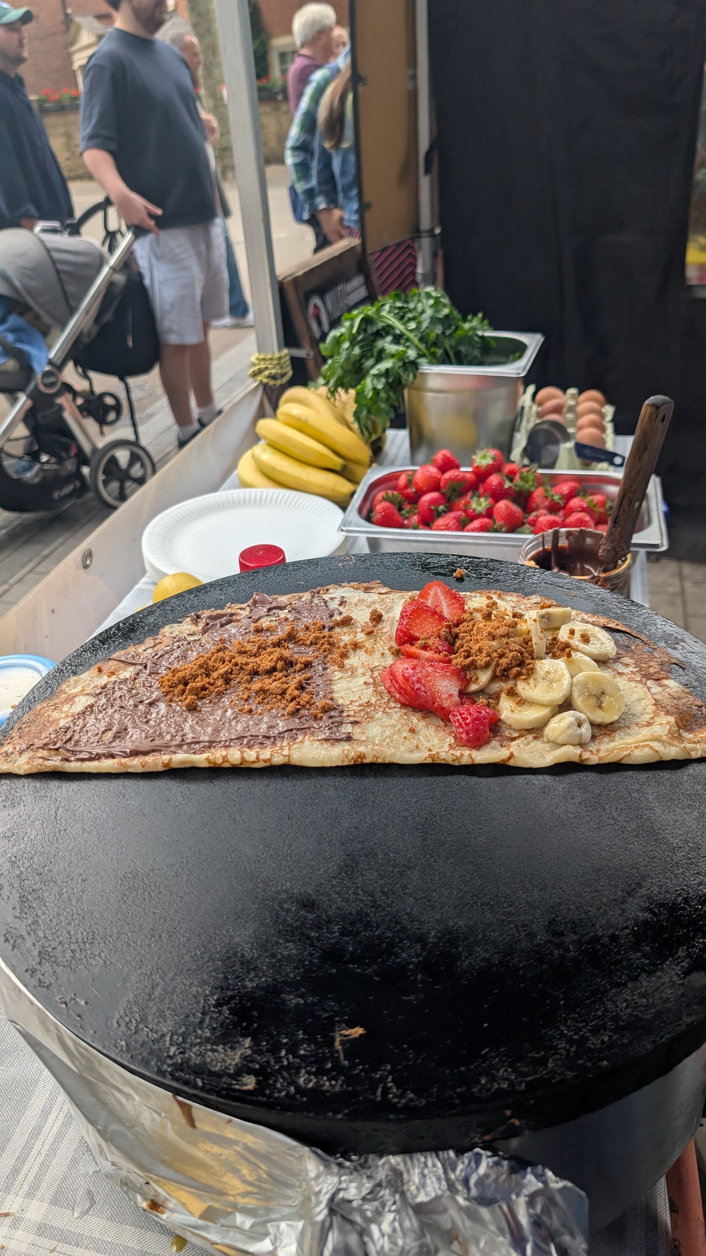 Sweet crêpe with Nutella, strawberries, banana and speculoos crumb, served live at a London street event with bananas and strawberries on display